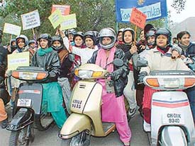 Girls wearing helmets take part in a scooter rally