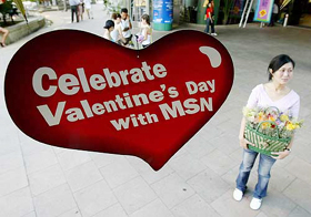 A woman carries a basket of flowers for sale near a Valentine's Day promotional sign outside a shopping mall