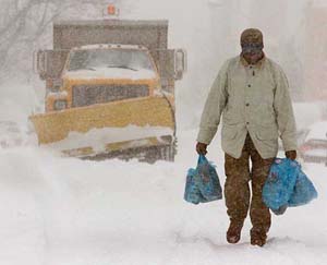An unidentified pedestrian carrying his groceries walks past a snow plough 