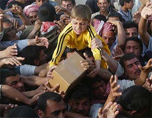 A child sitting on his fathers shoulders fights for a box of food