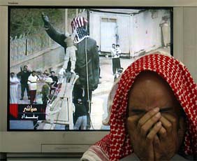 A Jordanian in Amman covers his face in front of a television showing a US Marine covering the face of a statue of Saddam Hussein with a US flag
