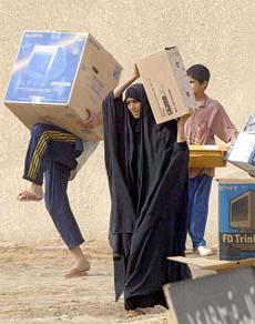 Iraqi civilians carry cardboard boxes as they loot a government warehouse