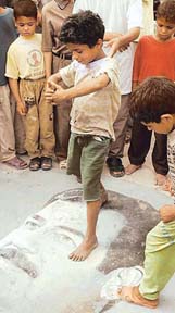 Local Iraqi children stand on an image of Saddam Hussein in Basra on Tuesday