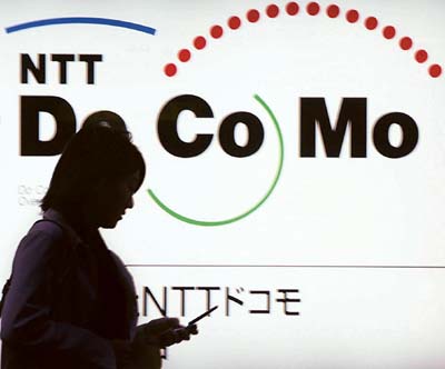 A Japanese woman is silhouetted as she uses a mobile phone in front of the NTT DoCoMo office.