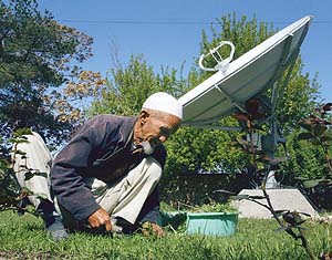 A gardener, Koka Abdullah, cuts grass in front of a large satellite dish at a house in Kabul.