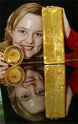 A girl holds a 12.5 kg gold bar and a 1-kg gold coin worth $141,240 and $10,272, respectively, at the Australian Stock Exchange in Sydney