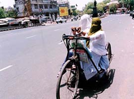 Two physically handicapped girlsride on a cycle with their face covered to avoid the hit wave