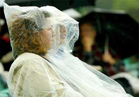 Spectators cover themselves with raincoats as rain delays the start of play at the Wimbledon Tennis championships