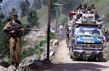A BSF soldier stands guard as a convoy of buses carrying pilgrims drive by