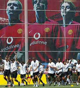 The Manchester United squad trains in front of a large advertisement of Paul Scholes Ruud van Nistelrooy and Ole Gunnar Solskjaer 
