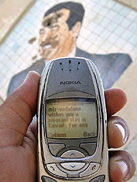 A man holds a mobile phone, connected to a Kuwaiti network, near a portrait of toppled leader Saddam Hussein