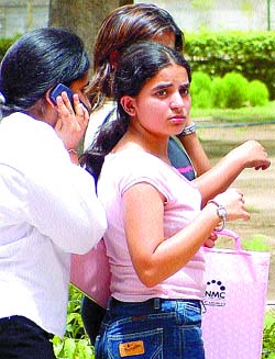 A college fresher uses her mobile on the sly even as her batchmate keeps a watchful eye, in view of the authorities cracking down on cell buffs