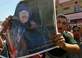 A man holds a picture of Saddam Hussein, as he shouts anti-US slogans