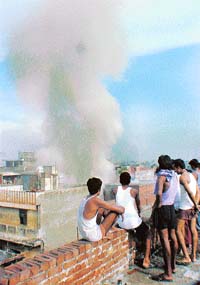 Onlookers watch the smoke coming out of a factory that caught fire in Ganesh Nagar