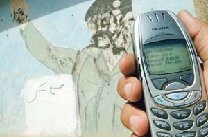 An Iraqi holds a mobile telephone, connected to a Kuwaiti network, near a portrait of toppled leader Saddam Hussein in the capital Baghdad