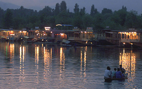 Tourists sit in a shikara as lights from nearby houseboats get reflected on the water of Dal Lake