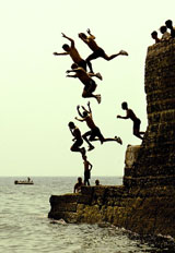 Youths jump into the sea from a small pier