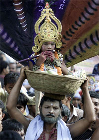A Bangladeshi devotee carries a young boy dressed as Lord Krishna 