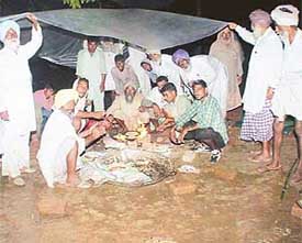 A group of farmers protects itself in rain on the second day of their protest dharna