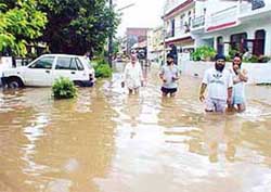 Residents of Phase V, SAS Nagar, wade through knee-deep water on a road flooded due to heavy rain on Wednesday morning