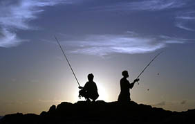 Men fish off a cliff at the sunset
