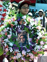 An Afghan girl carries a bouquet of flowers to put in front of a poster of Ahmad Shah Masood