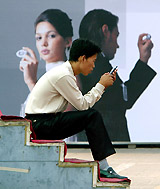 A man studies the functions of his new mobile phone in front of an advertisement for a mobile phone company in Beijing 