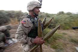 A US soldier carries confiscated rocket propelled grenades onto an army truck at an orchard on the outskirts of Tikrit, near Baghdad
