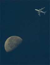 A plane flies over New Delhi with the moon in the background.