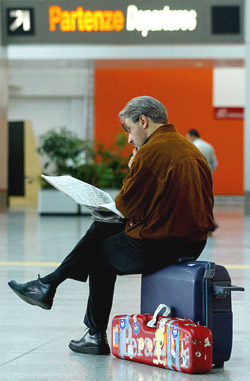 A commuter reads a newspaper as he sits on his luggage at Fiumicino Airport in Rome 