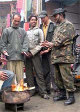 A CRPF jawan joins locals near a fire lit by shopkeepers on the main road in Srinagar to keep himself warm 