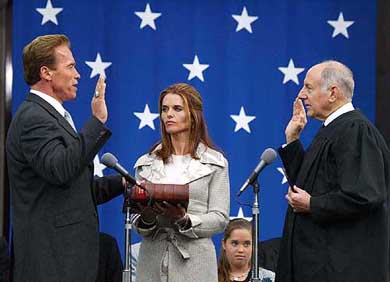 Californias newly elected Governor Arnold Schwarzenegger takes the oath of office as his wife Maria Shriver holds the Bible