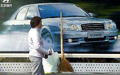 A woman waits for a shuttle in front of a poster promoting Sonata, a car made by Sino-South Korean Hyundai, at a bus stop in Shanghai 