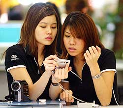 Two salesgirls take a closer look at their digital camera at a booth in a shopping mall in Kuala Lumpur on Monday