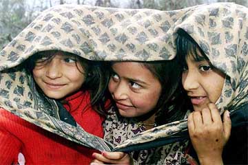 Girls huddle under a shawl to protect themselves from cold in Jammu
