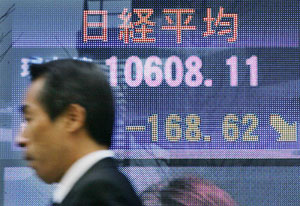 A businessman walks past an electronic board displaying the Nikkei average