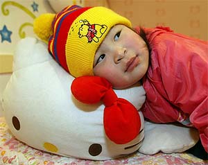A Japanese girl, wearing a Winnie the Pooh hat, relaxes atop a Hello Kitty doll at Sanrio Puroland in Tokyo