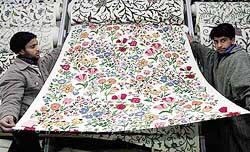 Two Kashmiri salesmen unroll fabric adorned with traditional embroidery at a shop in Srinagar