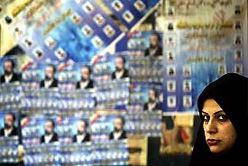  woman waits at a bus station smeared with election posters in Tehran