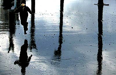A boy runs past reflected palm trees on seafront, which has been flooded by waves during a storm in Beirut 