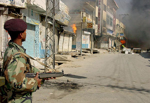 A Pakistani soldier watches burning shops