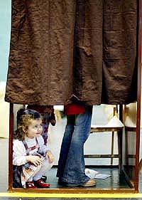 A little girl peeks out from a polling booth while her mother fills in her ballot in the Spanish general elections 