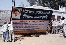 Workers remove a hoarding highlighting achievements of the Chautala government 