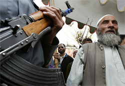 A policeman holds an AK-47 rifle as an elderly man listens to speakers during an election rally in Srinagar 