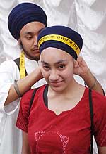 A member of 'Akal Purakh ki Fauj' helps an NRI girl tie her turban 
