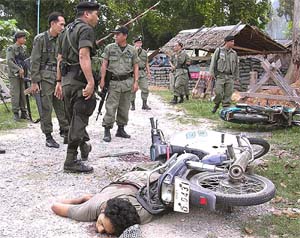 Thai security force personnel stand near a dead body