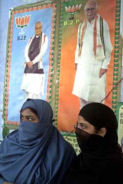 Muslim women stand in front of the posters of Prime Minister Atal Bihari Vajpayee and Deputy Prime Minister L.K. Advani 