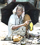 A cobbler protects himself from the sun with an umbrella and cloth on his head on Sunday as he mends shoes in Mumbai.