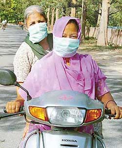 Two women riders cover their faces to escape the dust haze, which created breathing problems for many city residents. 