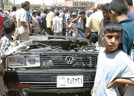 Iraqis crowd around a destroyed car after a US military tank ran over it in northern Baghdad on Tuesday. 